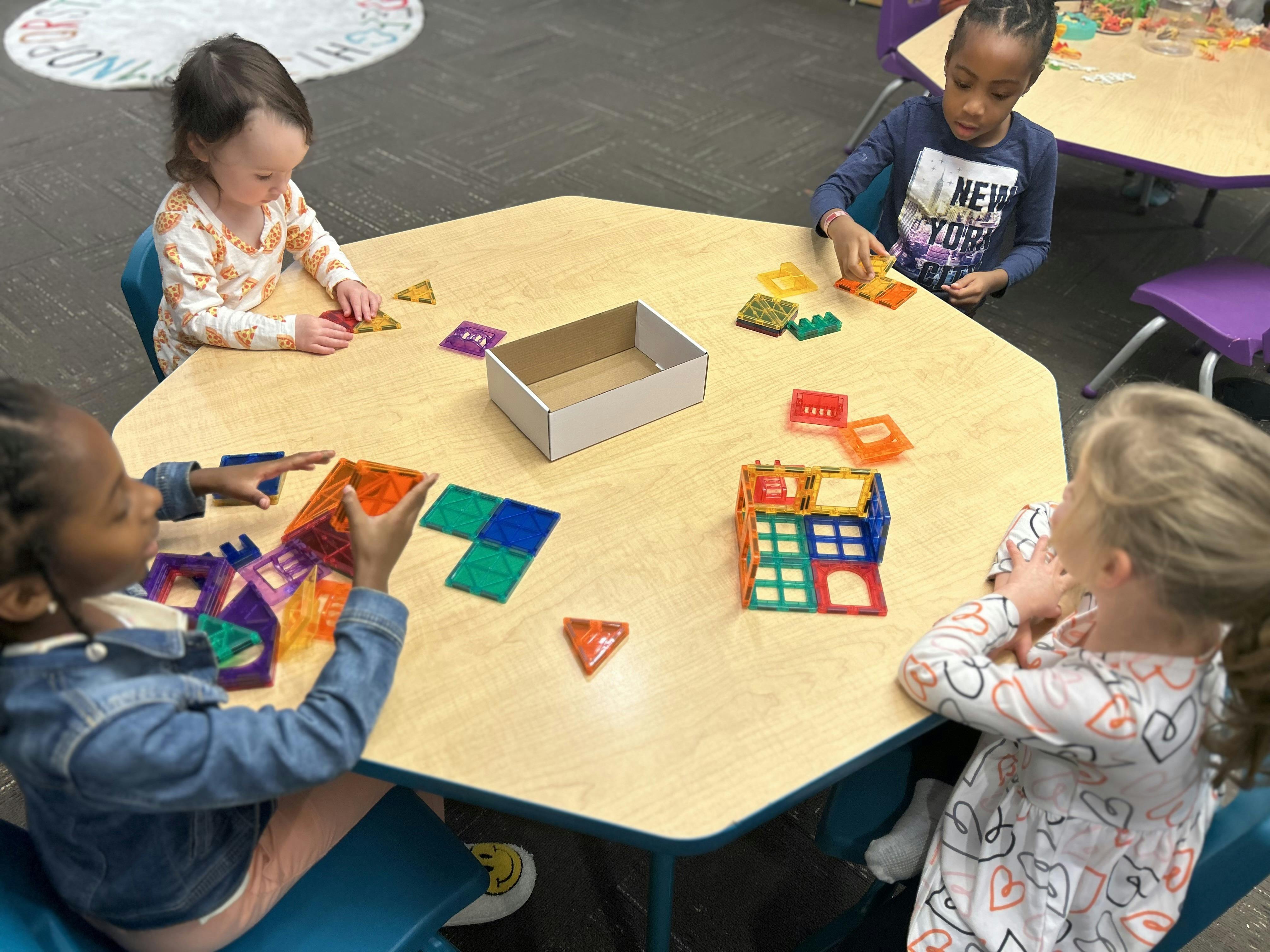 Four children sitting at a table building with colorful magnetic tiles