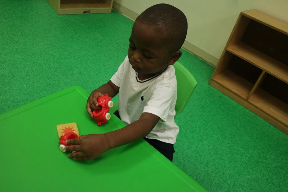 Child playing with red toy cars at a green table
