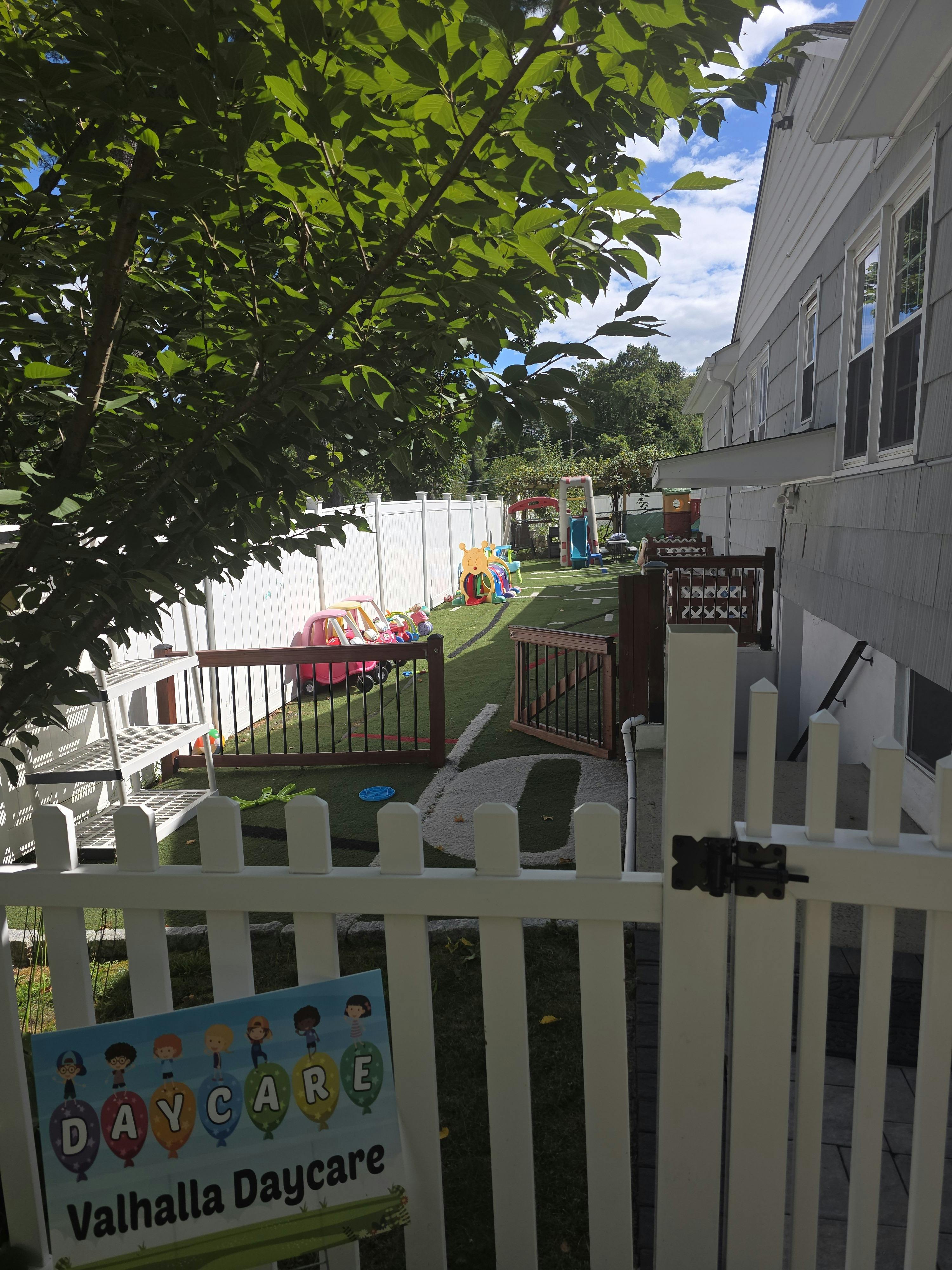 Daycare playground with a white fence and a sign that says Valhalla Daycare