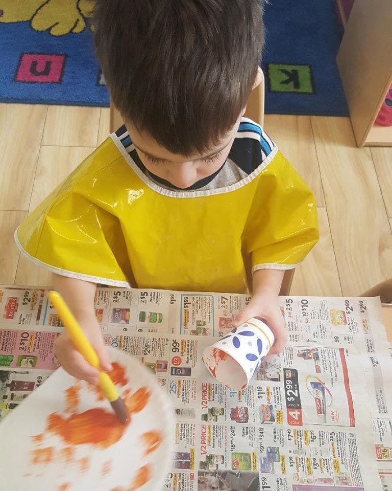 Child in a yellow smock painting a paper plate