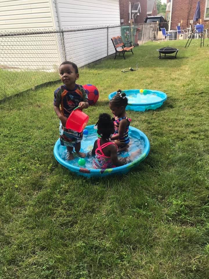 Three children playing in a small wading pool in a grassy yard
