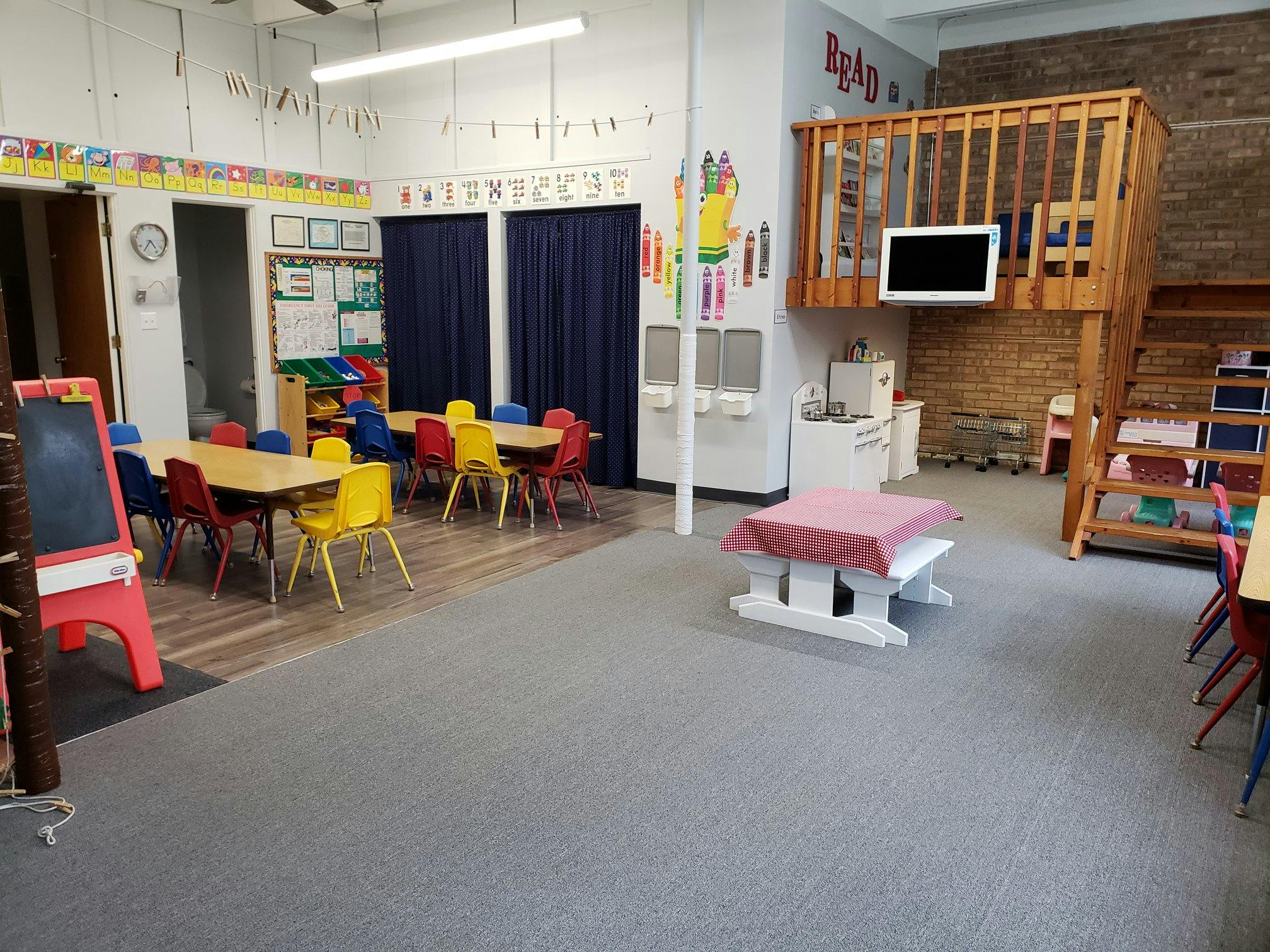 Classroom with small tables and chairs, and a wooden loft structure