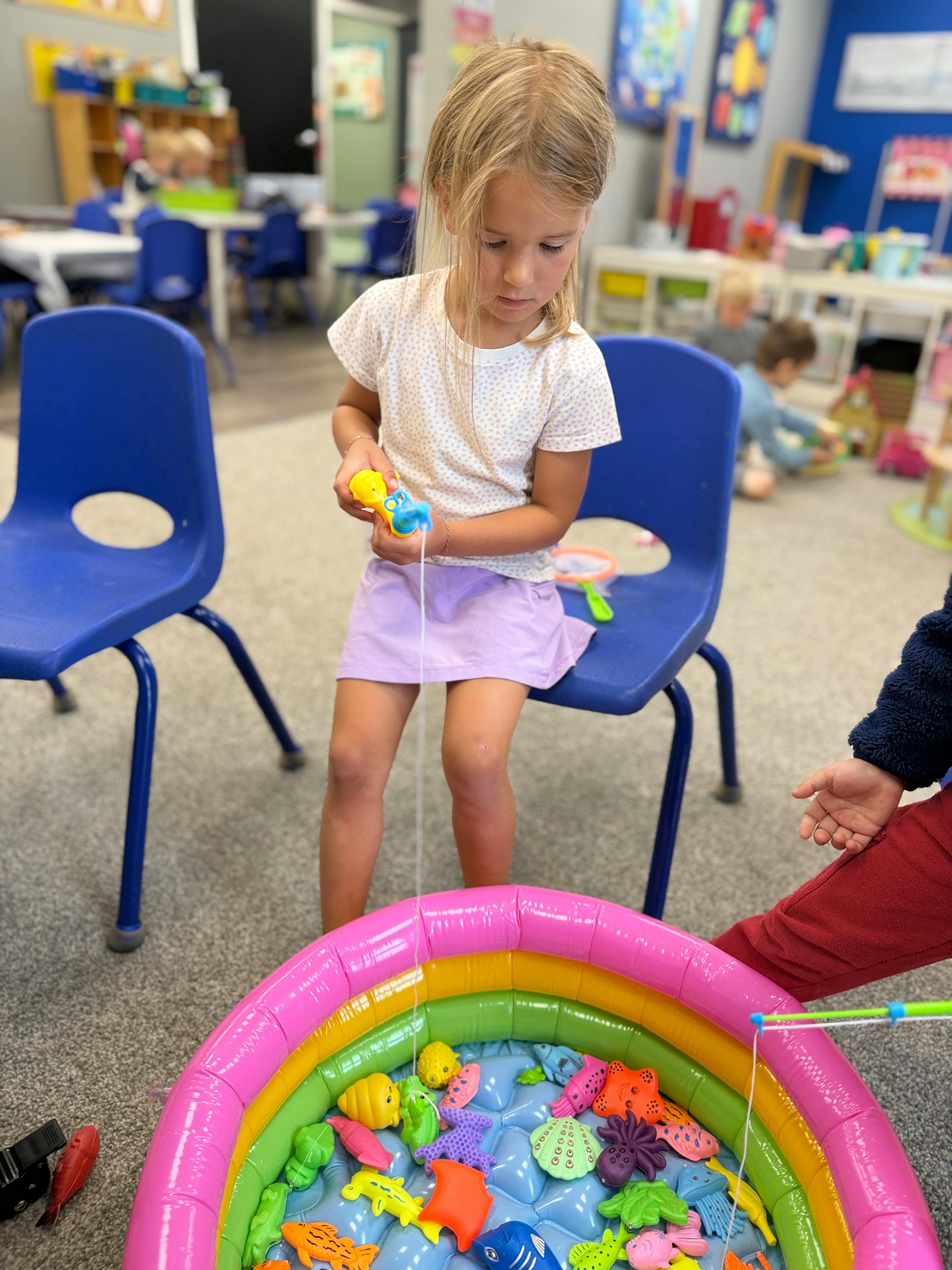 Child playing with a toy fishing rod in a small inflatable pool