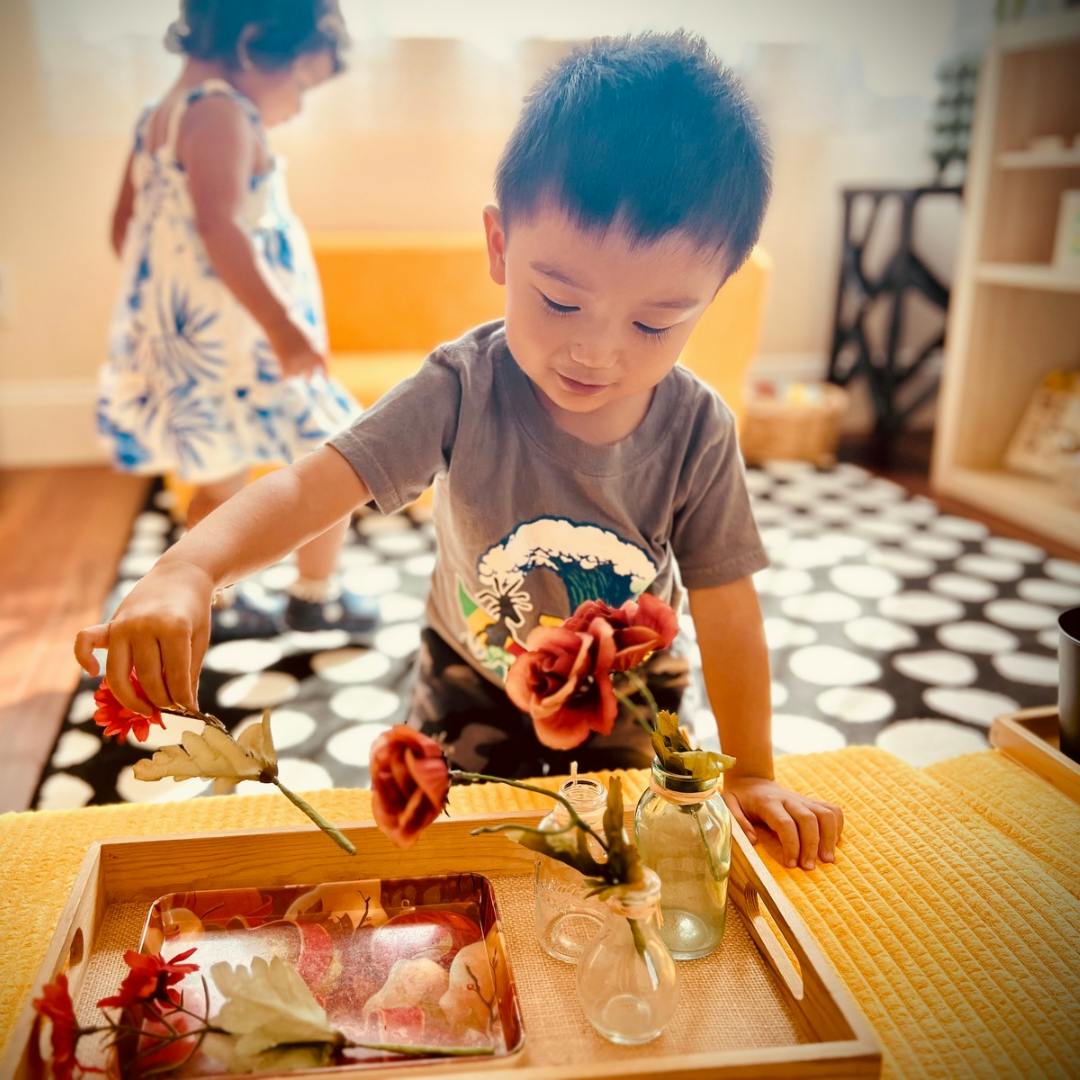 Child arranging flowers in small vases on a tray