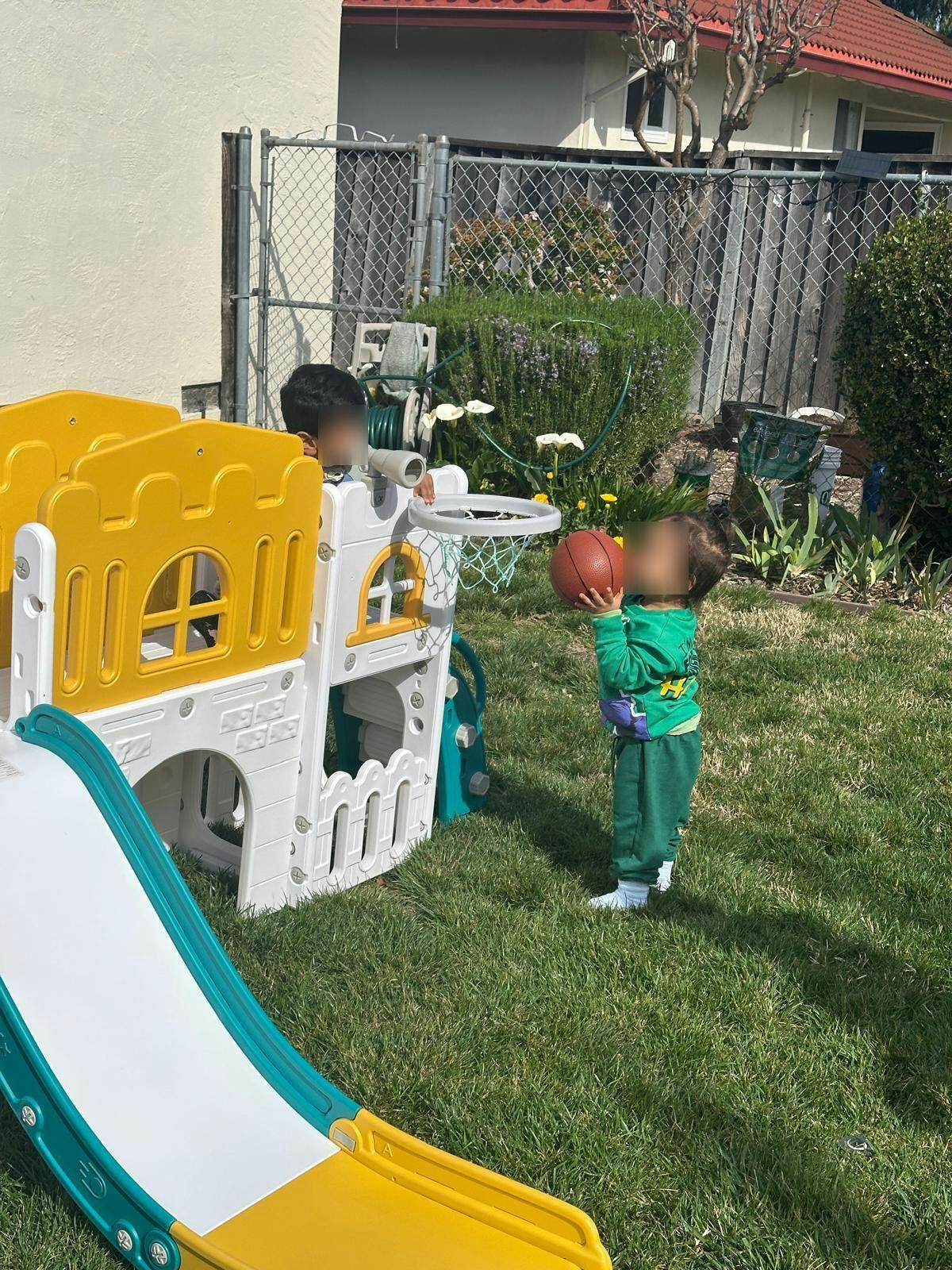 Two children playing with a basketball and a play structure in a yard