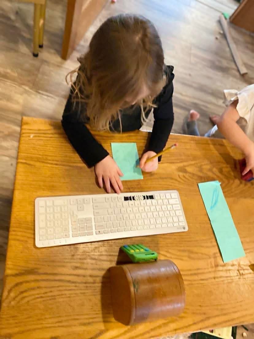 Child writing on paper at a desk with a computer keyboard