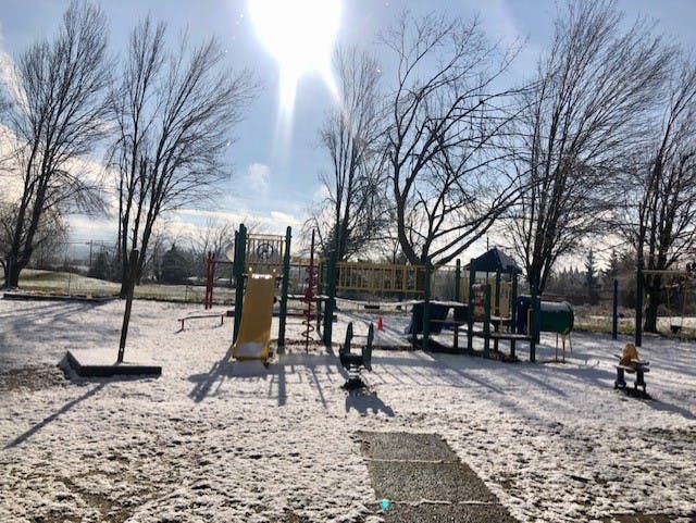 Playground covered in light snow with bare trees under a bright sky
