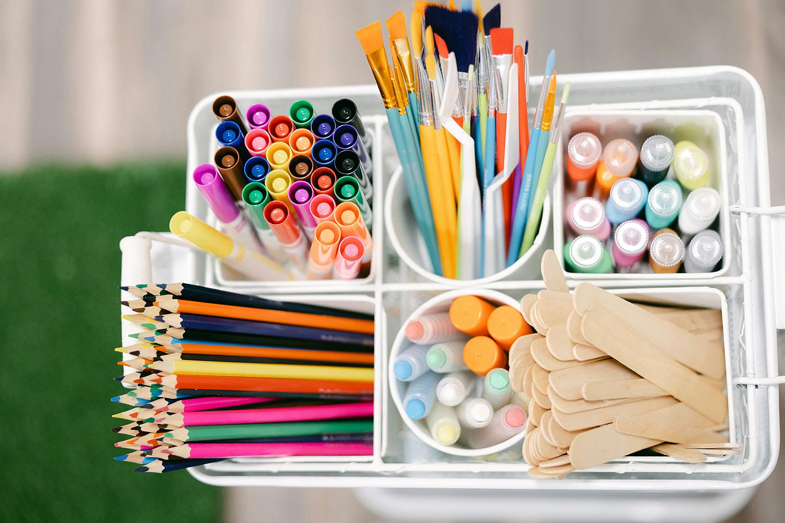 An art supply caddy filled with colorful markers, paint brushes, paint, and pencils