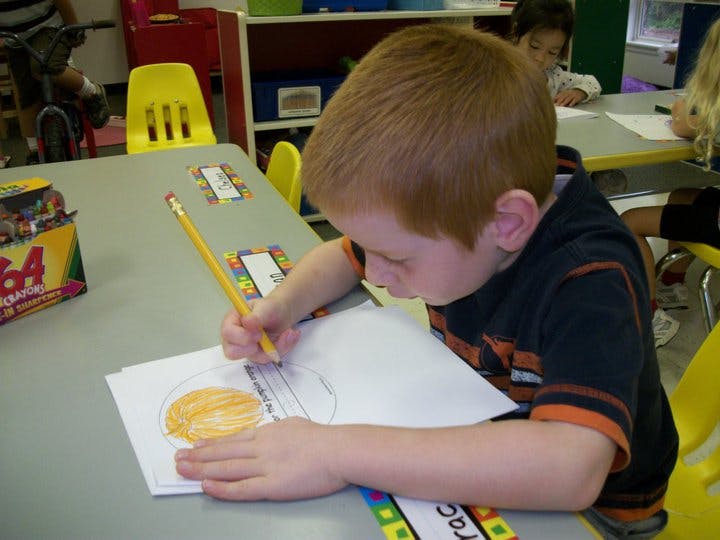 Child coloring a drawing at a table in a classroom