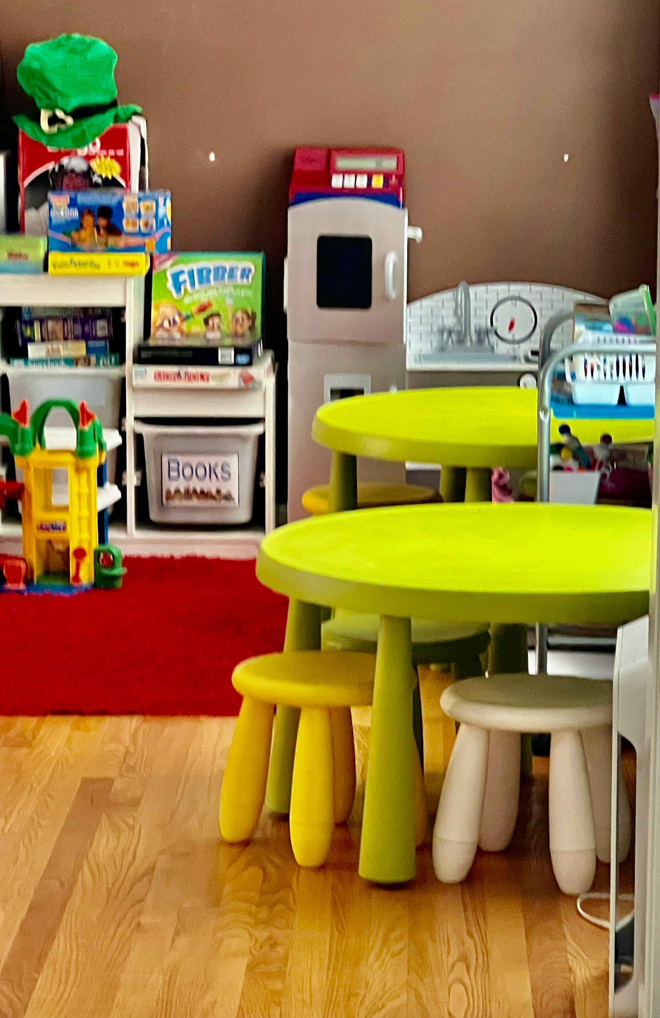 Playroom with small tables and chairs, toy kitchen, and book storage