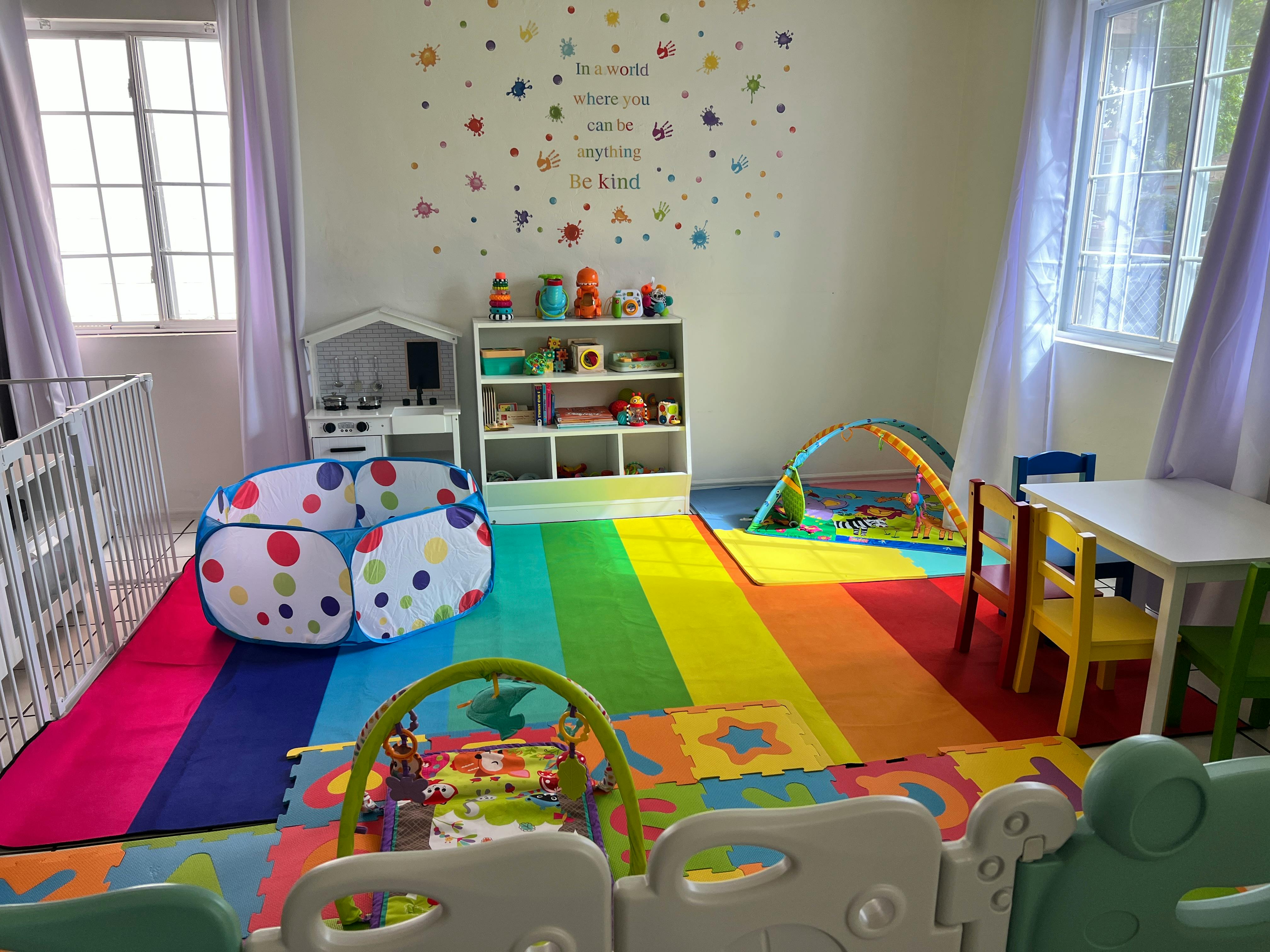 Playroom with colorful floor mats, crib, shelves with toys, and small table and chairs