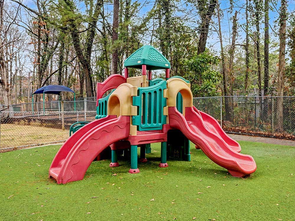 A red and green playground structure with multiple slides on green turf