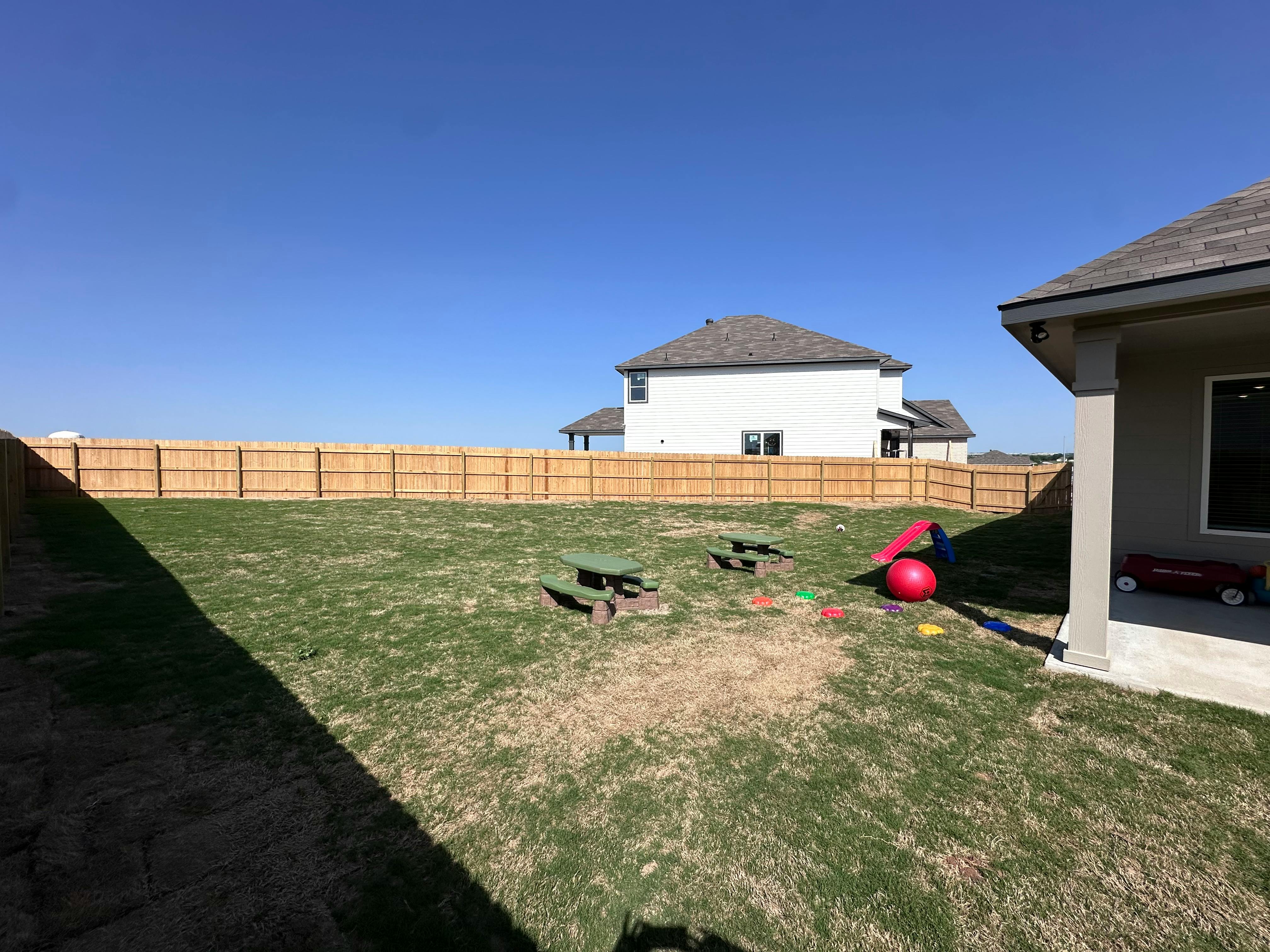 Backyard with a wooden fence, house, and play items