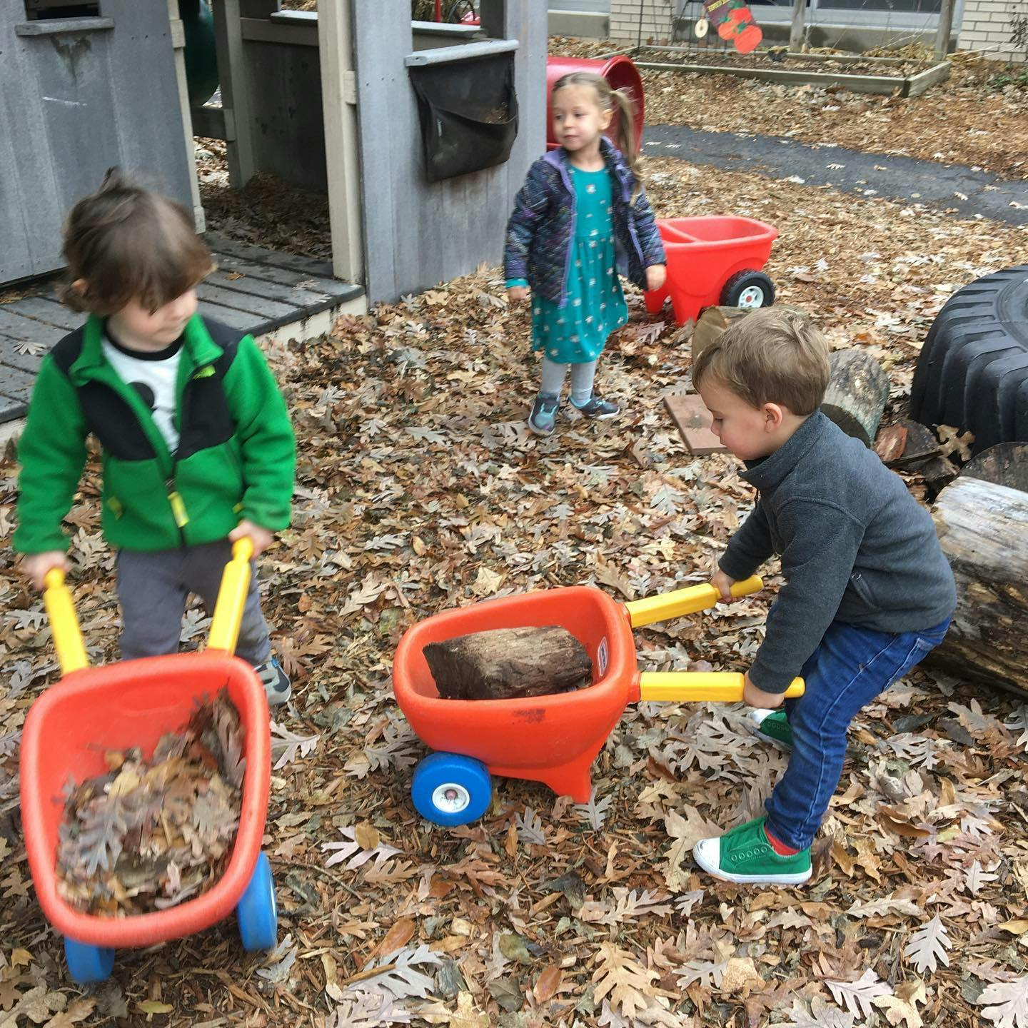 Three children playing with toy wheelbarrows outdoors