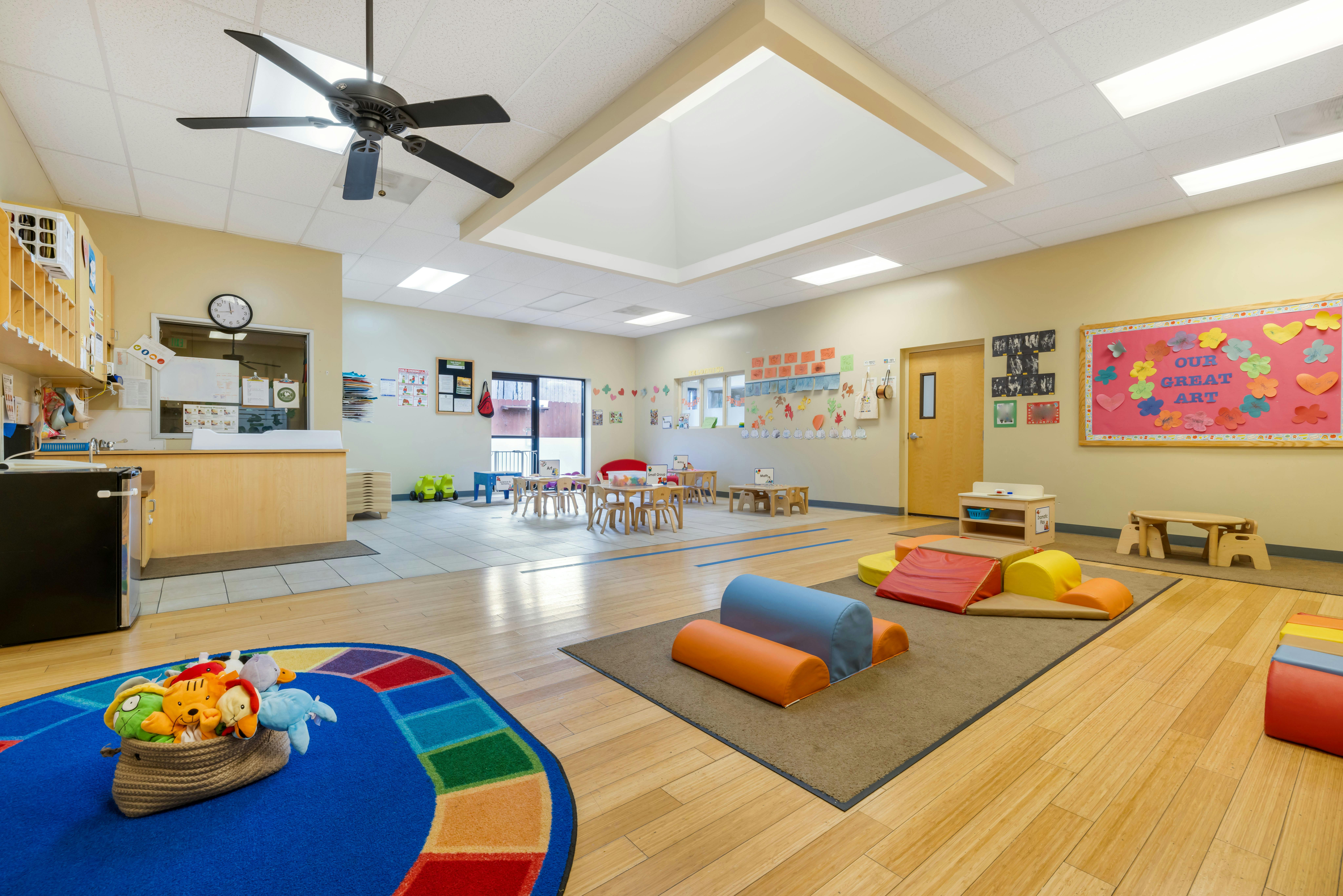 A colorful empty daycare classroom with small tables, chairs, and soft play equipment