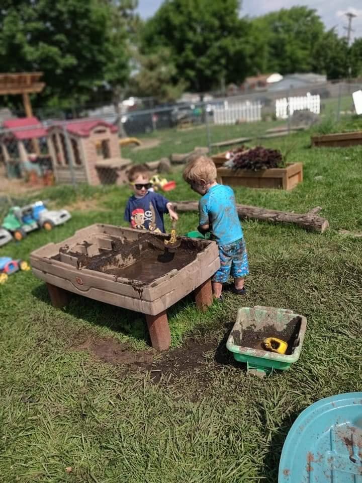 Two children playing in a mud table outdoors