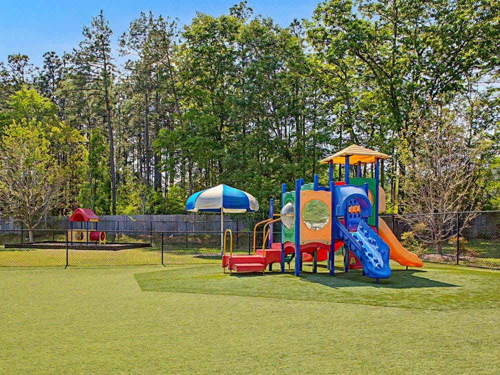 Colorful playground with slides and a small structure under a blue and white umbrella