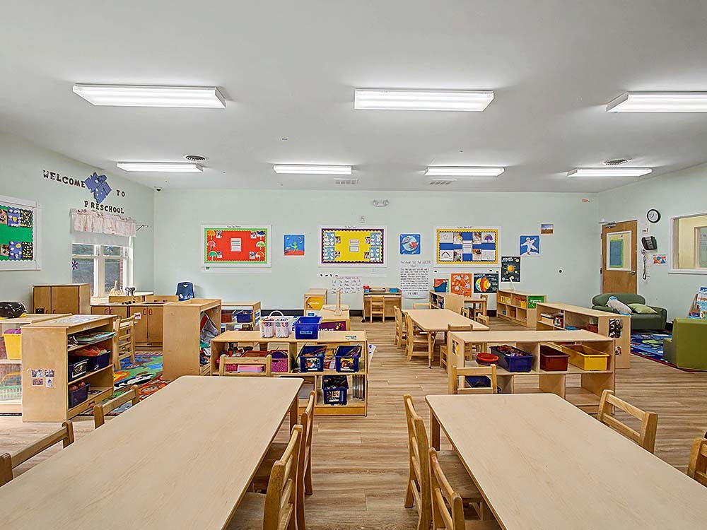 Empty preschool classroom with tables, chairs, and learning materials