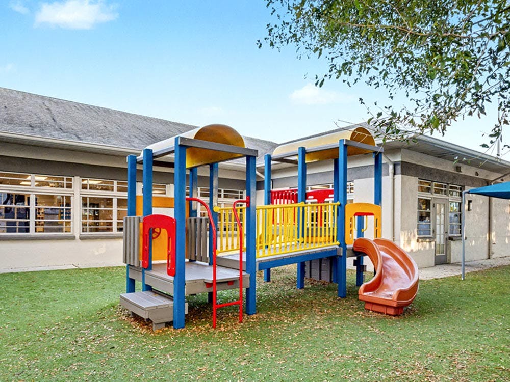 Colorful playground structure with a slide on green grass outside a building