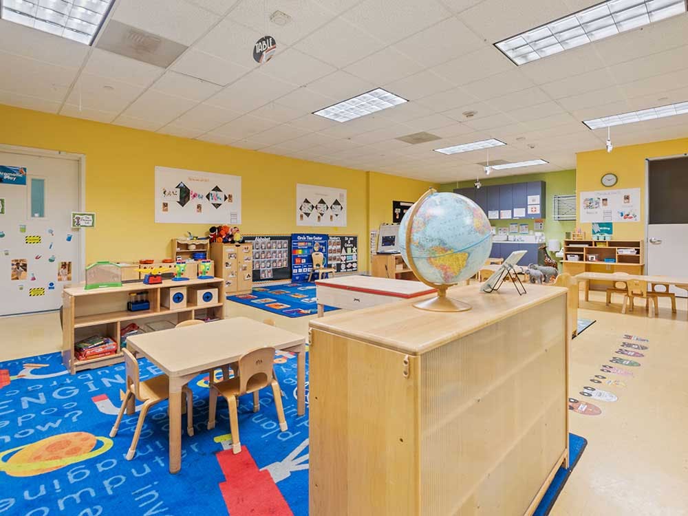 Classroom with yellow walls, a globe, small tables, and shelves with toys