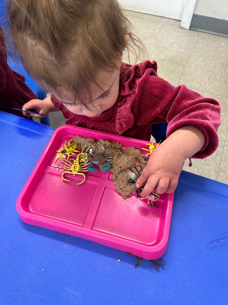 Child playing with toys in a pink tray