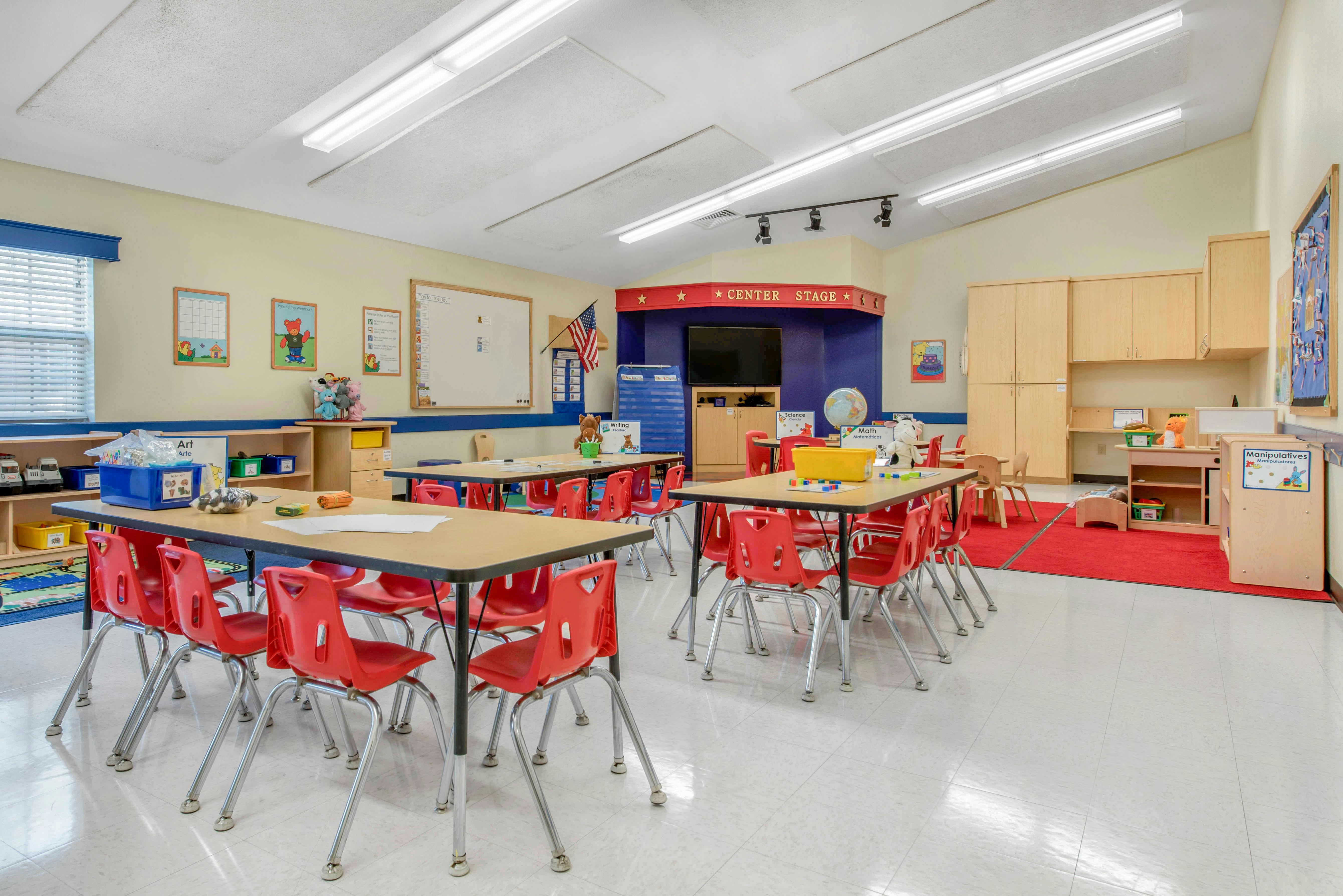 Classroom with child-sized tables and red chairs, a small stage, and activity areas