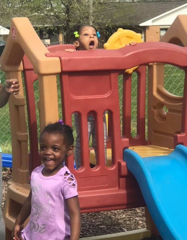 Two children playing on a red and brown playground structure with a blue slide