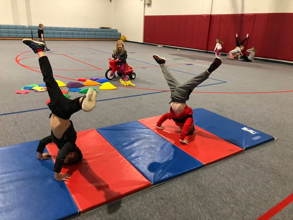 Two children doing handstands on mats in a gym