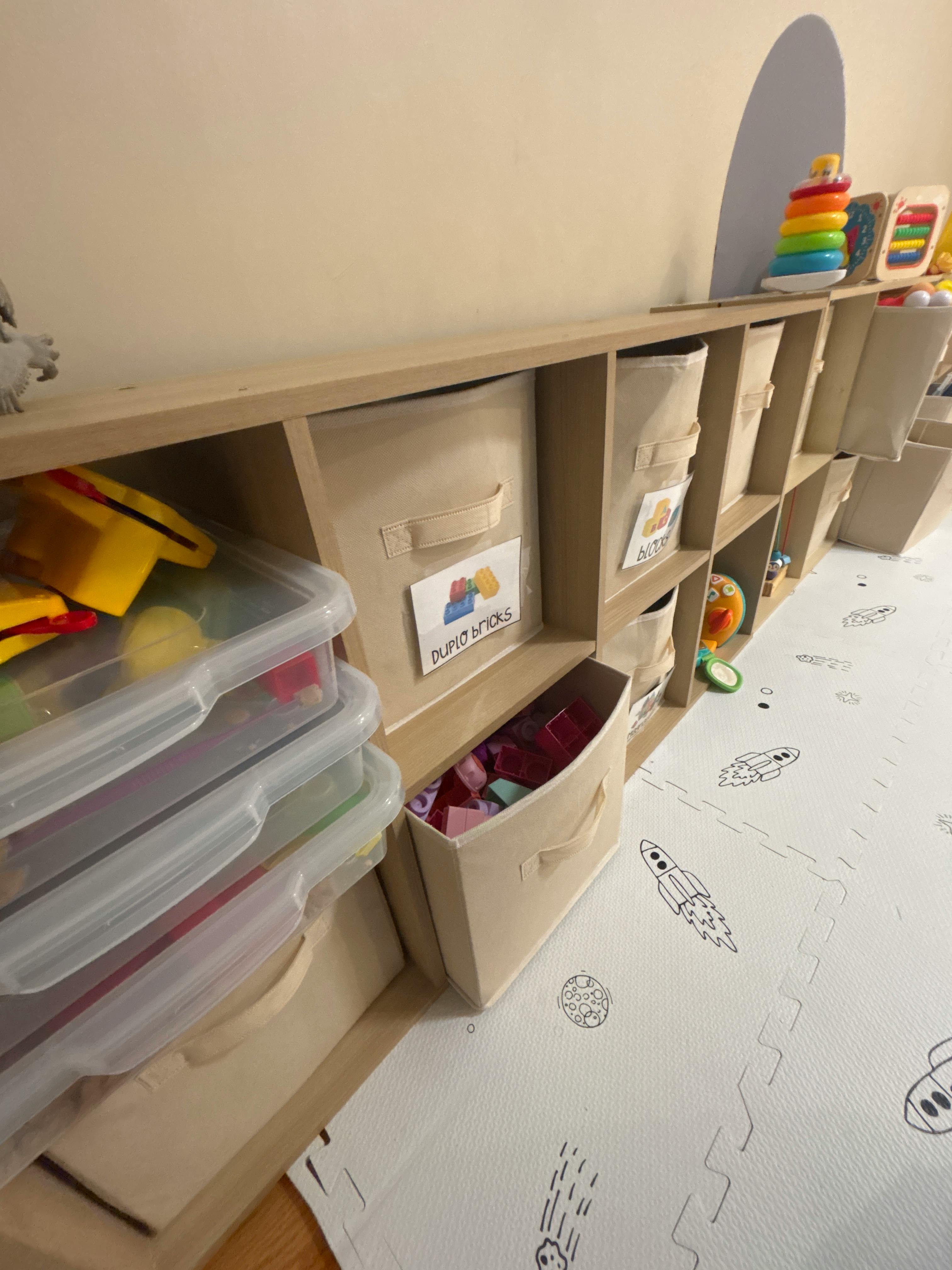 Wooden toy storage shelf with labeled fabric bins and plastic containers