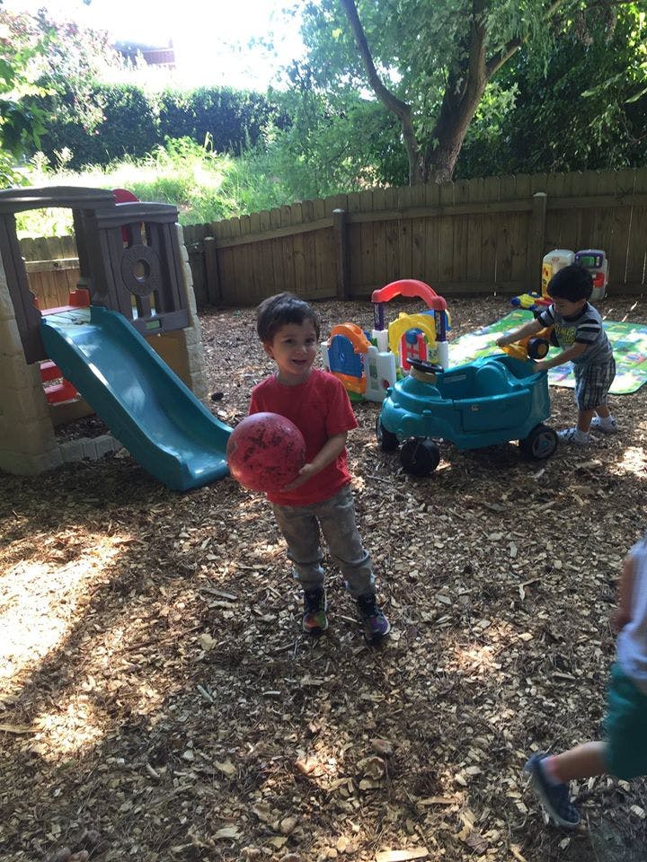 Child holding a red ball on a playground with other children and toys
