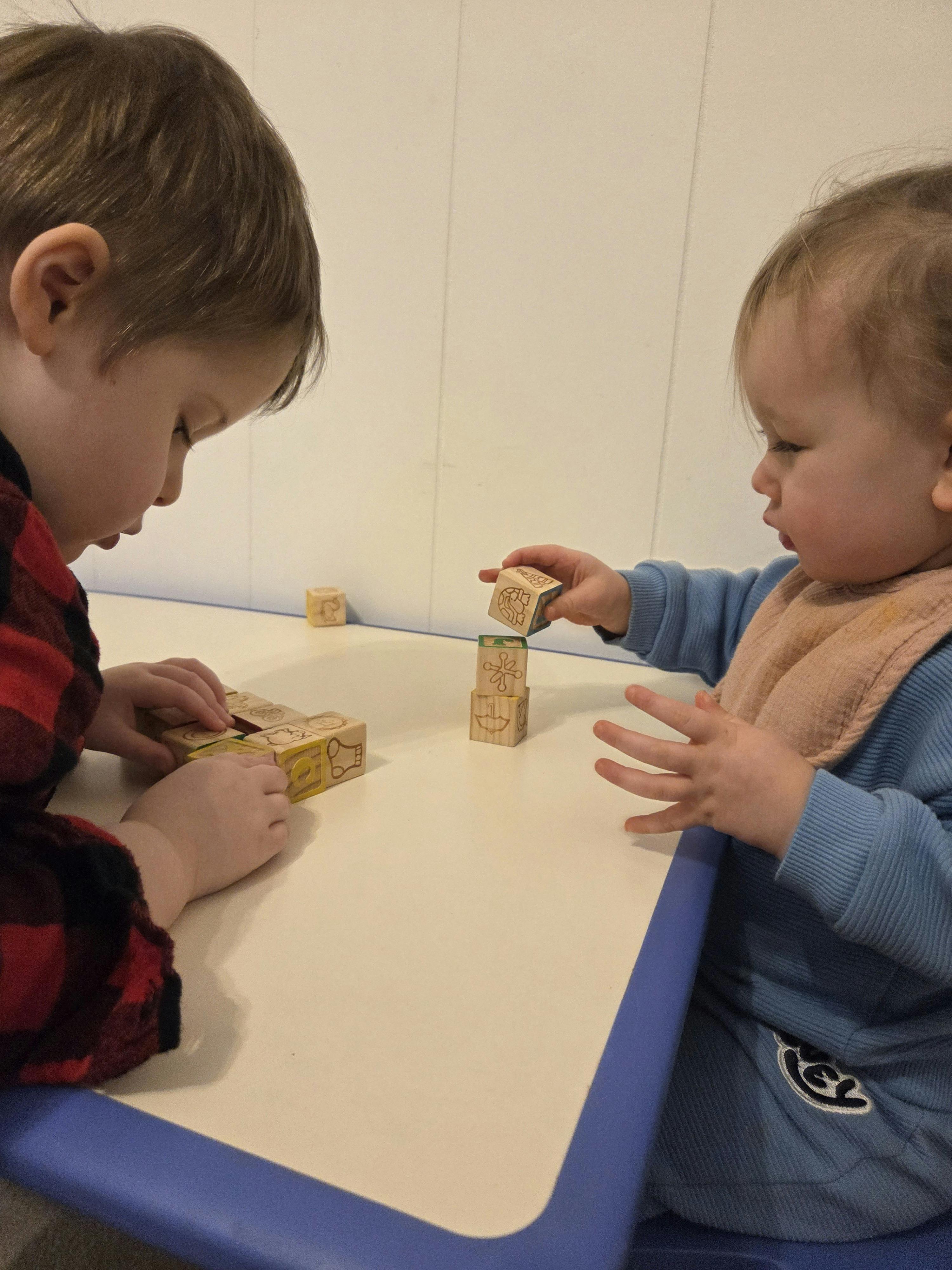 Two children playing with wooden blocks at a table