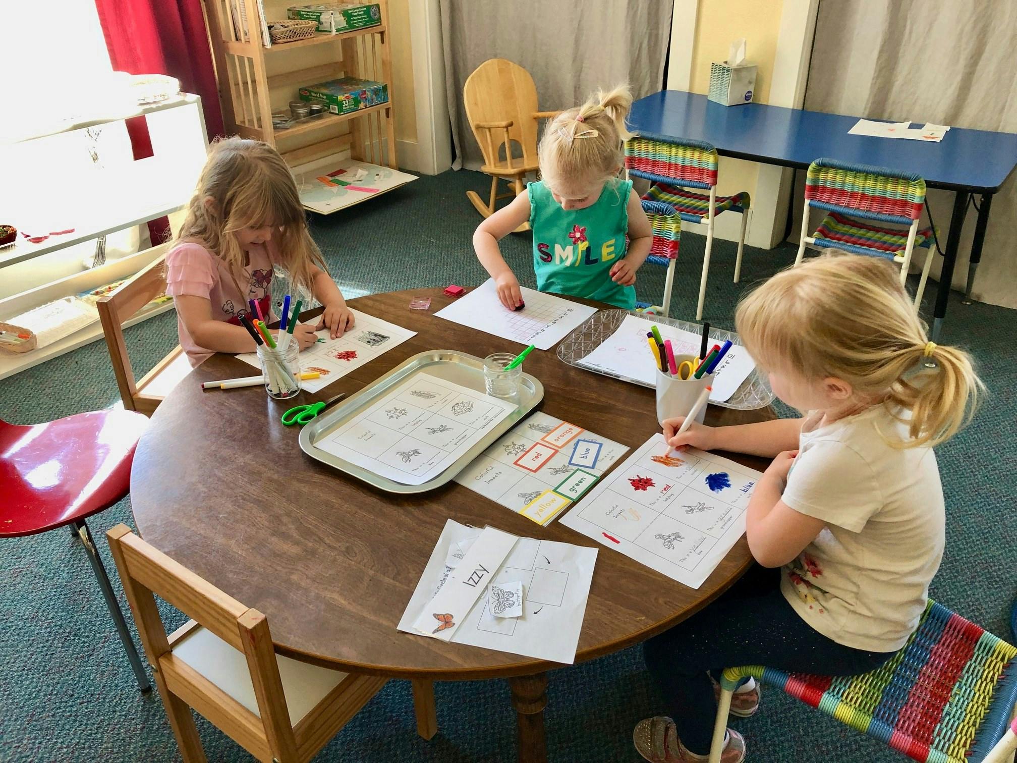 Three children drawing and coloring at a table in a classroom