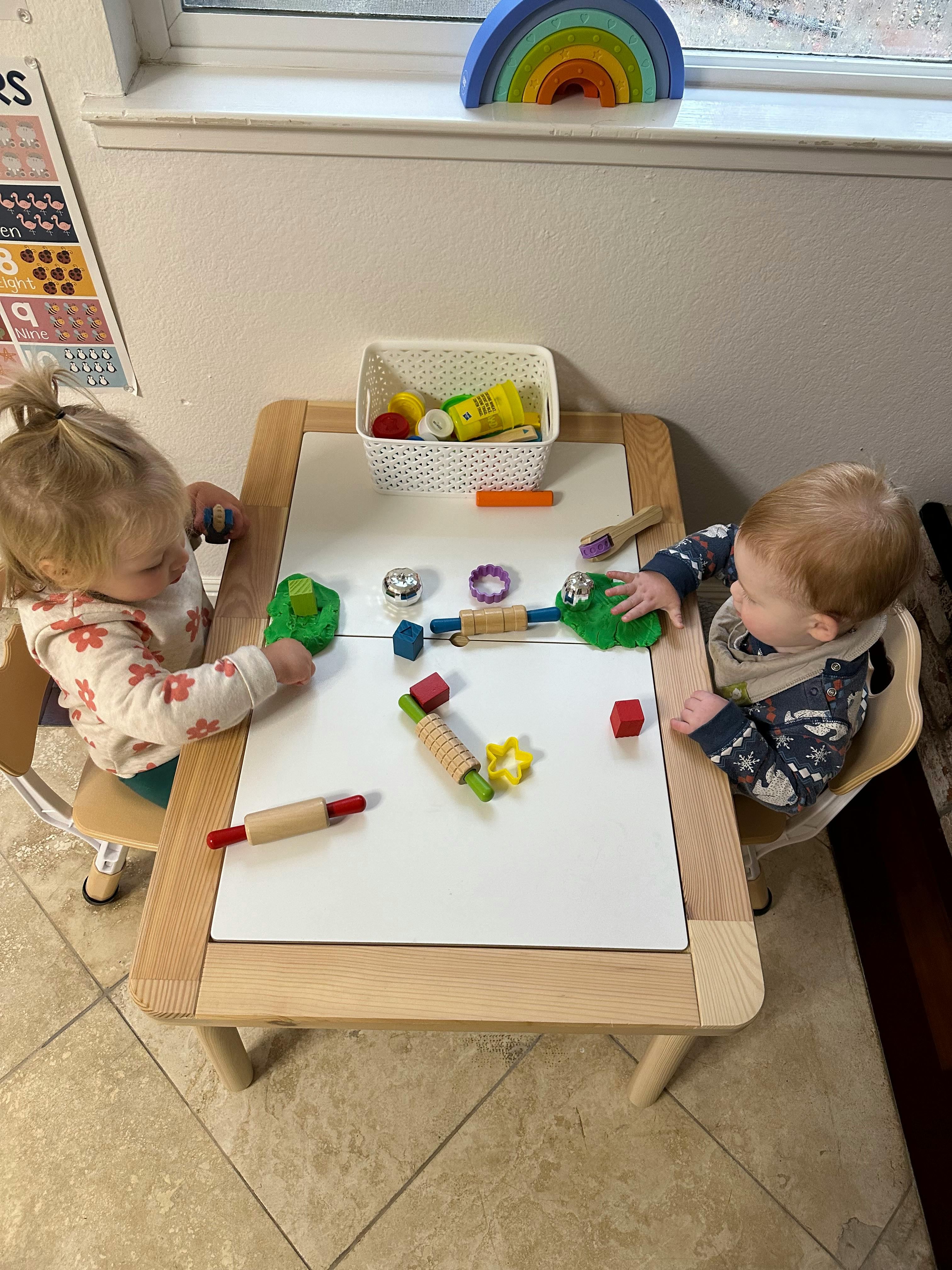 Two children playing with modeling clay and toys at a table