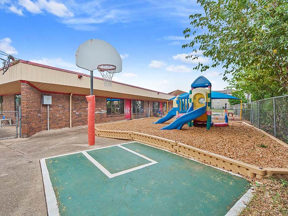 Playground area outside a brick building with a basketball hoop and play structure