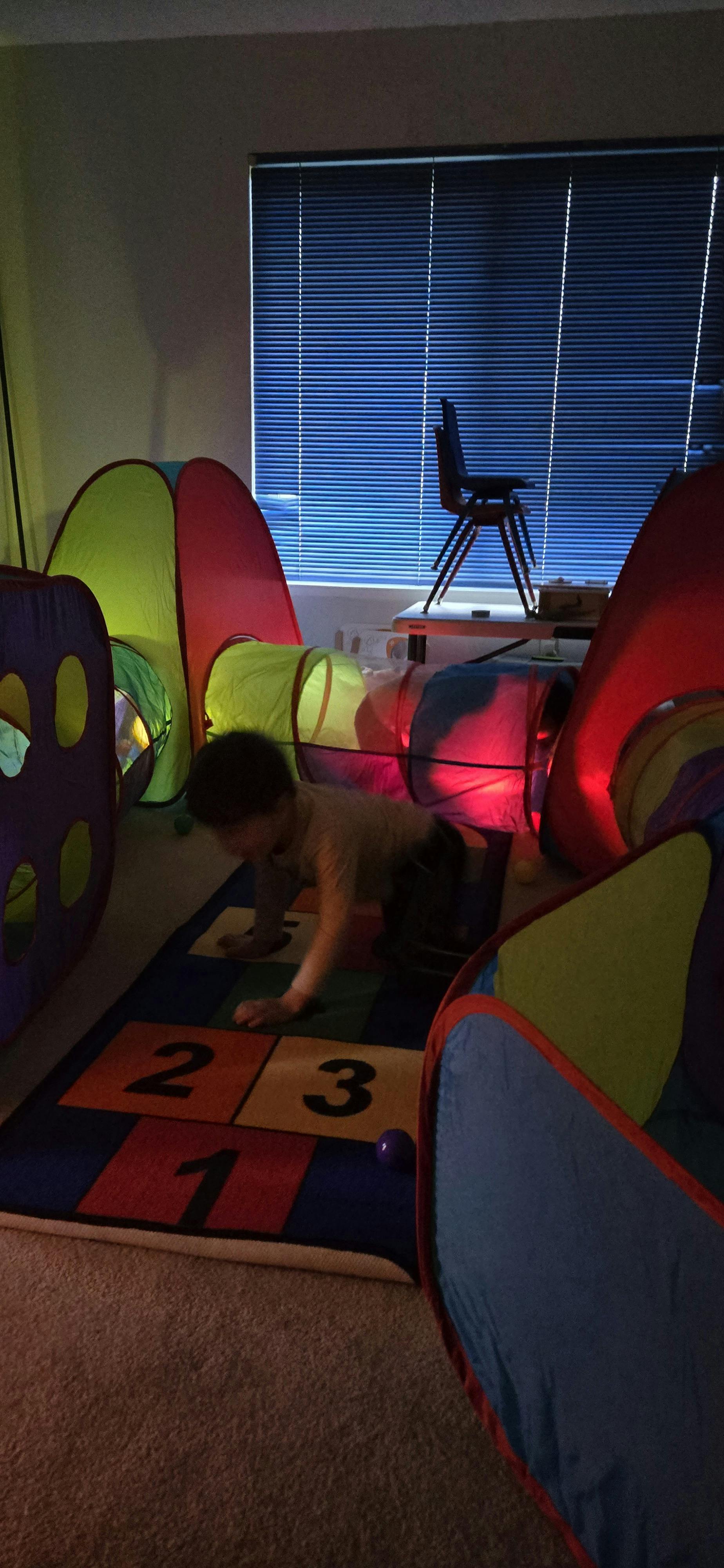 Child crawling through a colorful play tunnel on a number mat