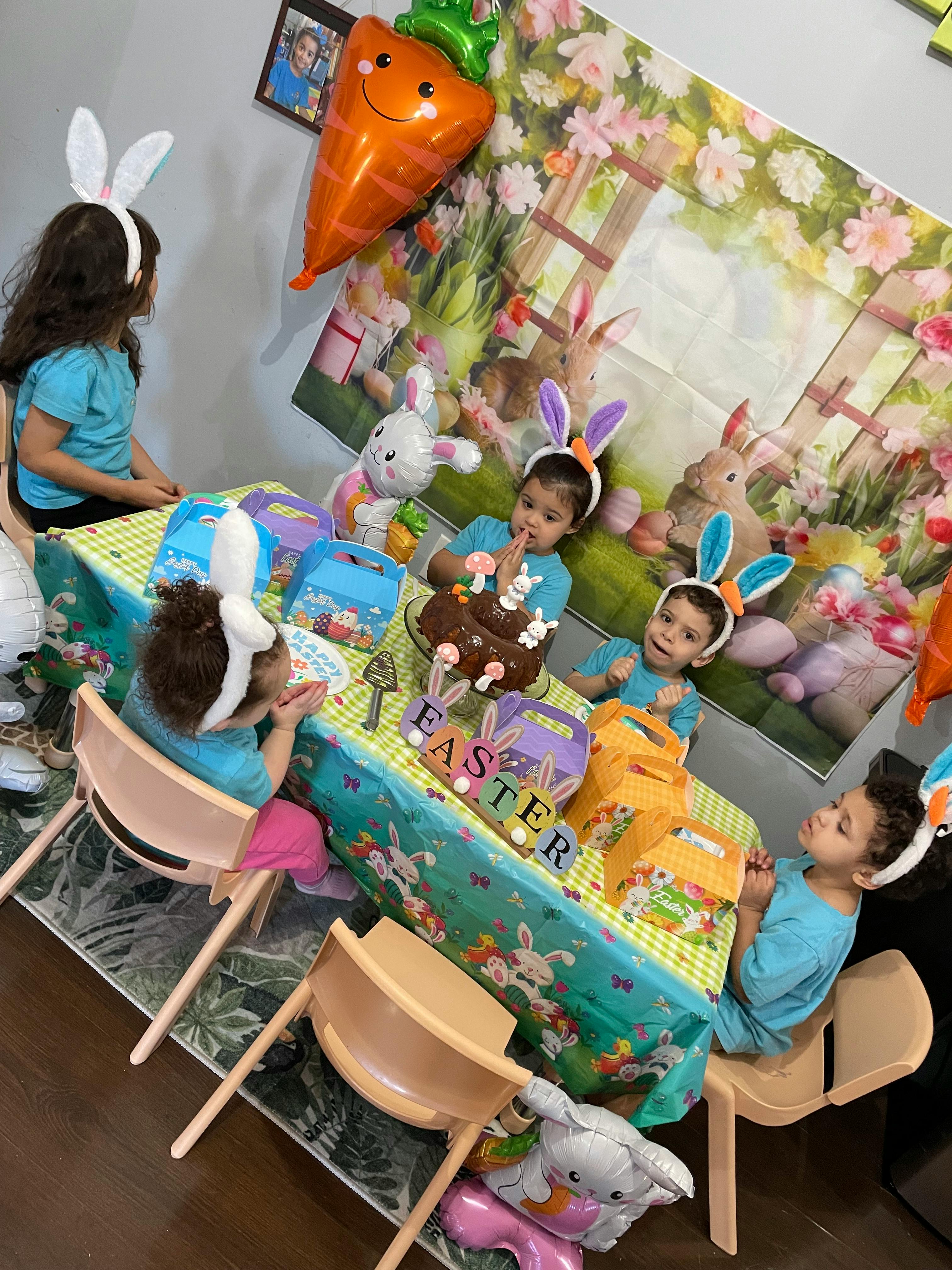 Children wearing bunny ears sitting around a table with a cake and decorations
