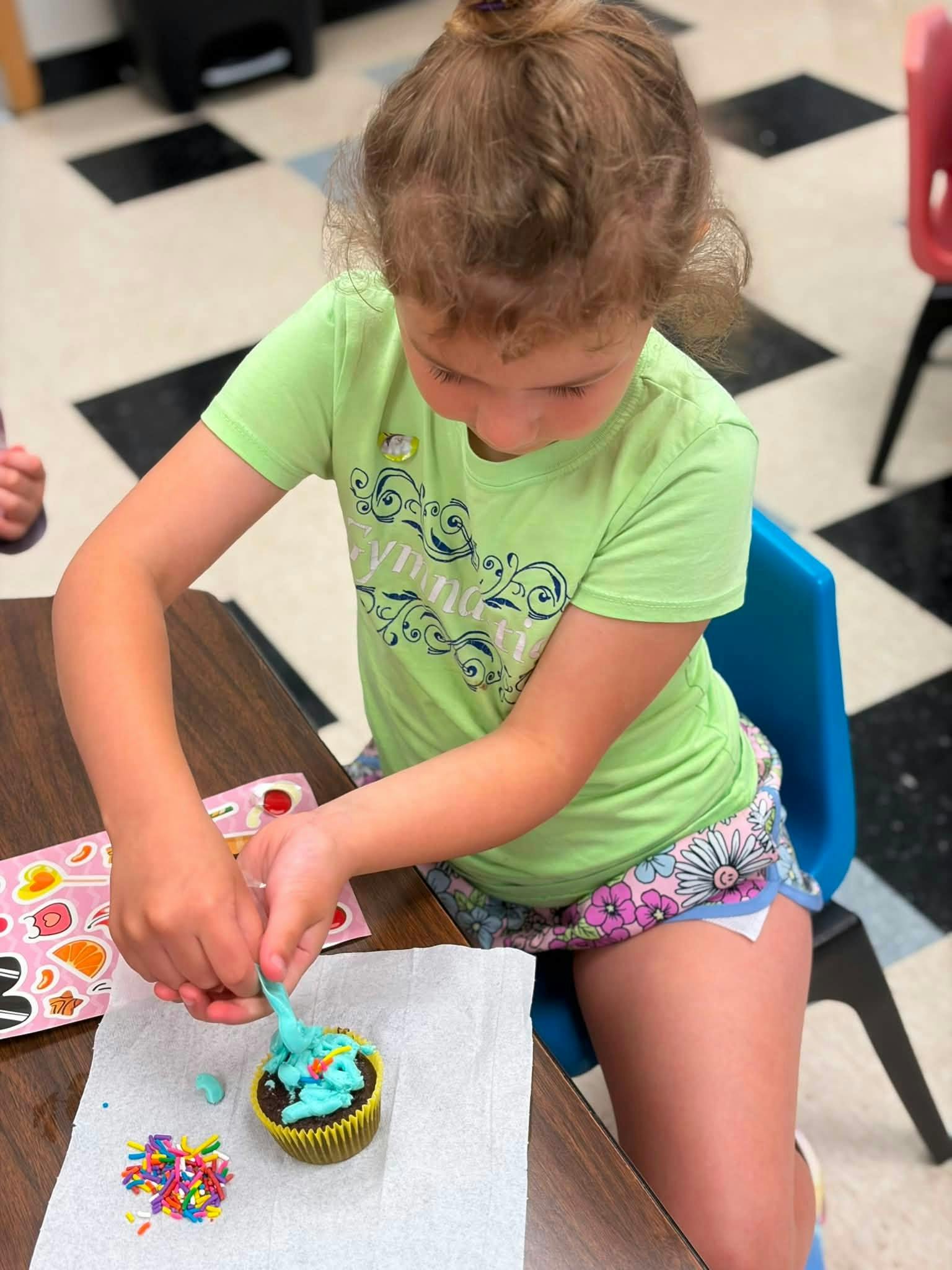 Child decorating a cupcake with frosting and sprinkles at a table