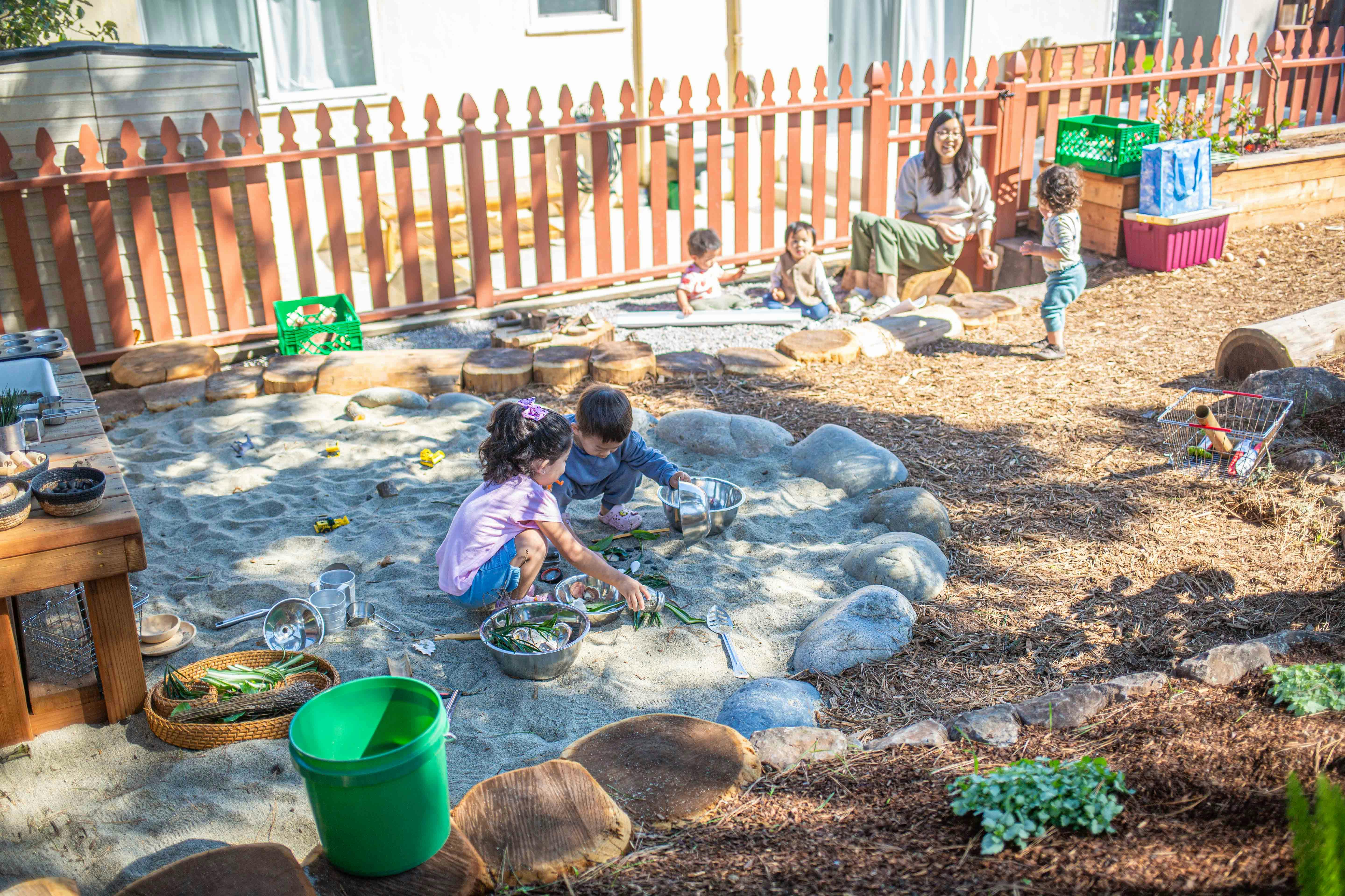 Children playing in a sandbox with an adult supervising nearby