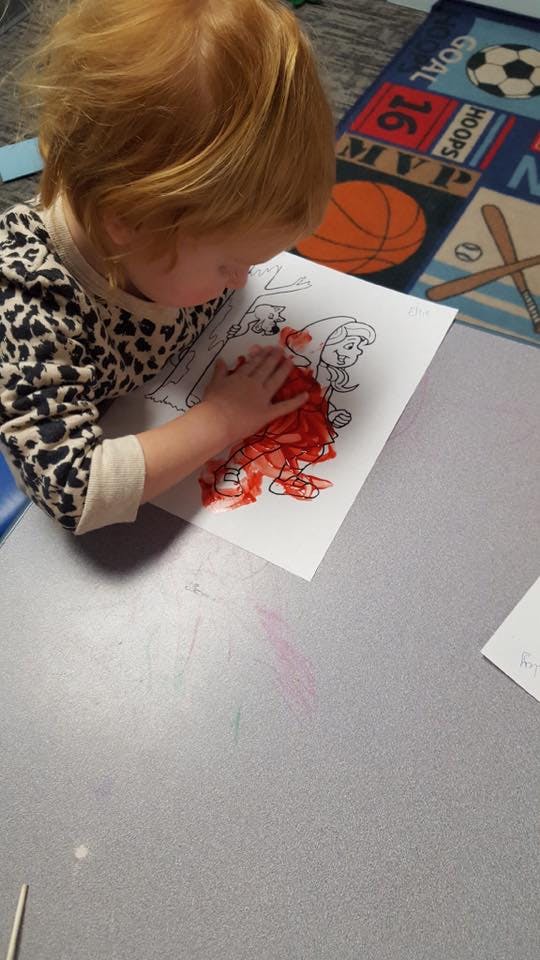 Child coloring a drawing with red crayon