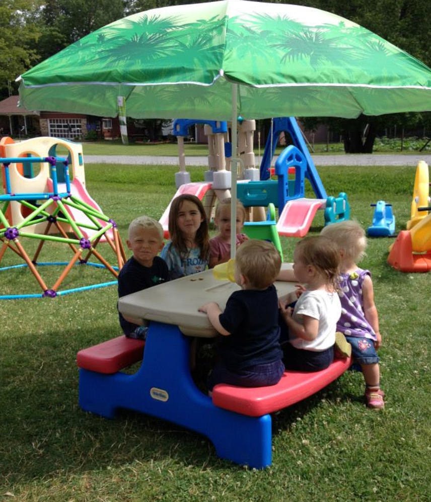 Children sitting at a picnic table under an umbrella