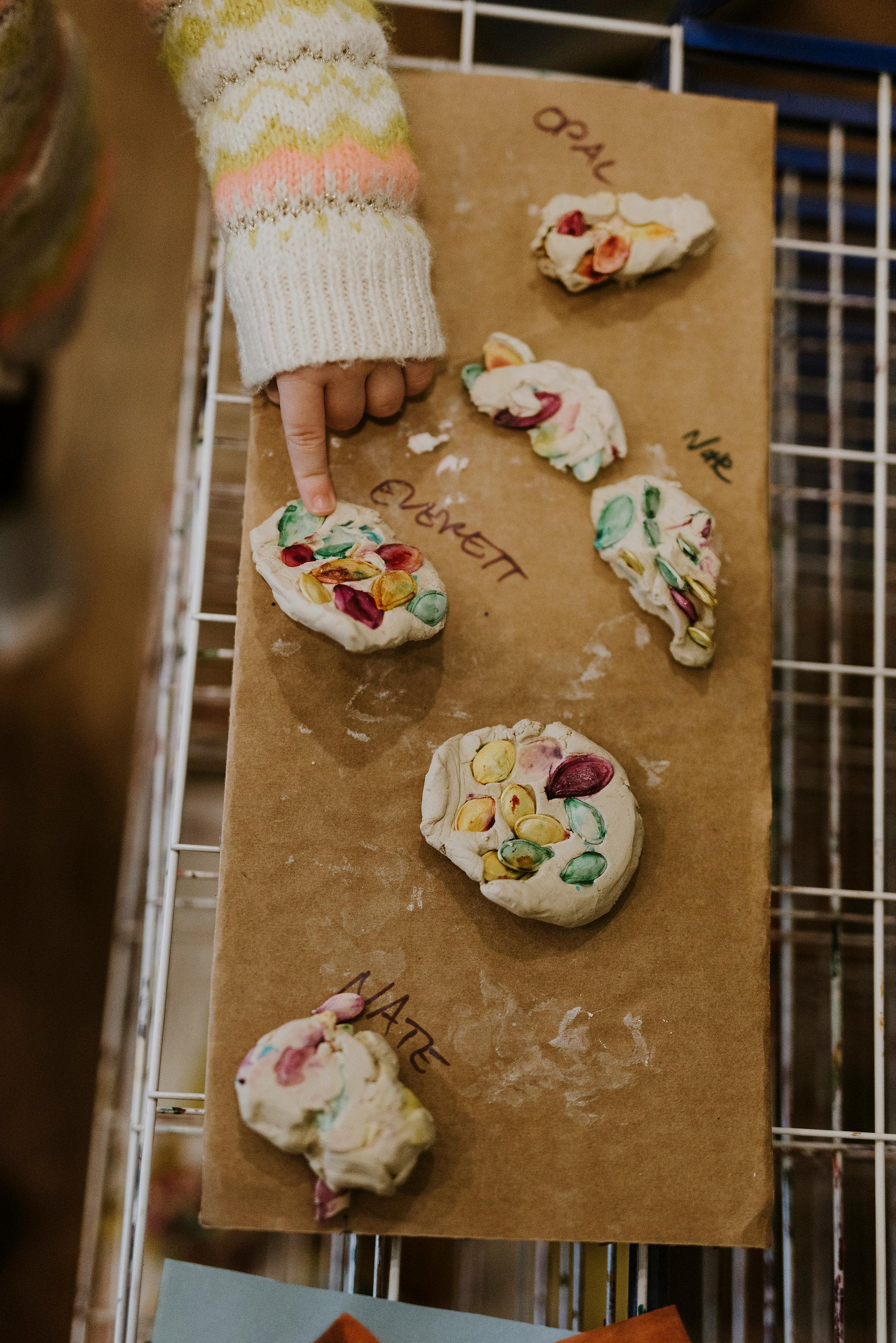 Child's hand pointing to a clay creation with colorful beads
