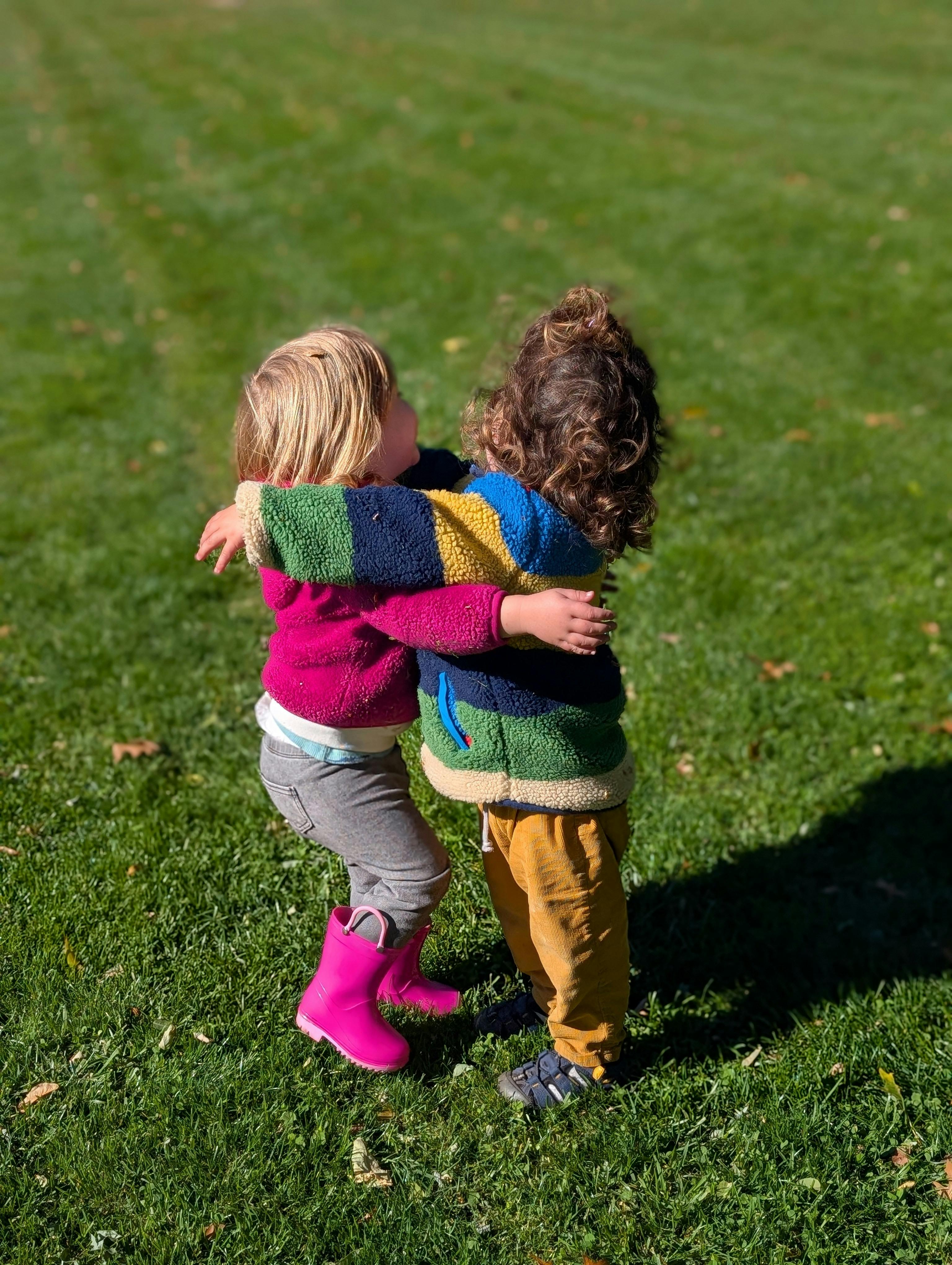 Two children hugging outdoors on grass