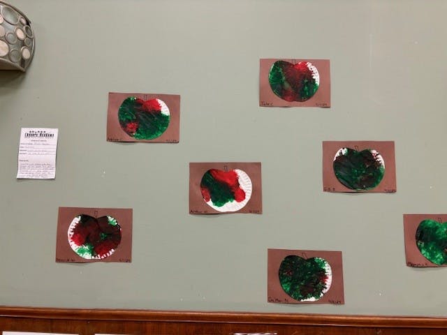 Children's artwork with red and green paint on brown paper displayed on a wall