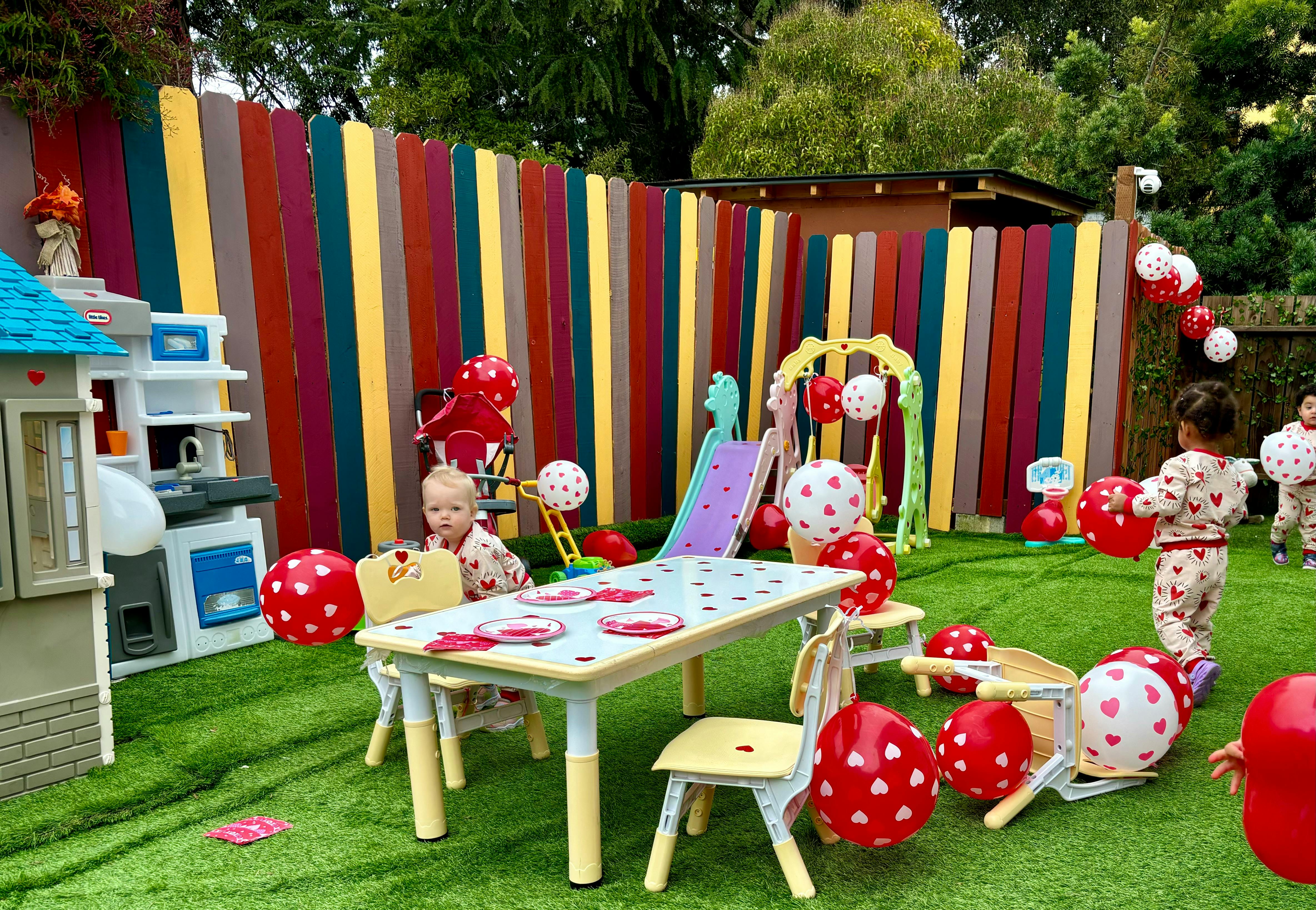 Child sitting at a table in a yard with balloons and play equipment