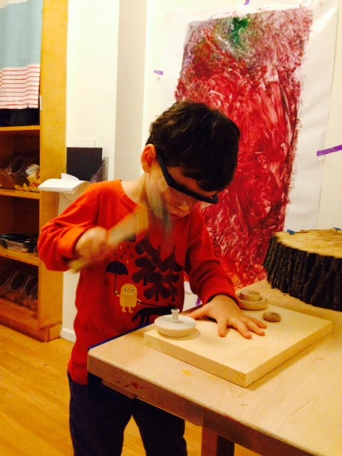 Child wearing safety glasses hammering a wooden peg into a board