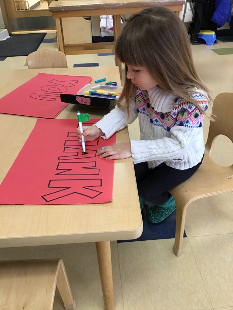 Child writing on red paper at a table