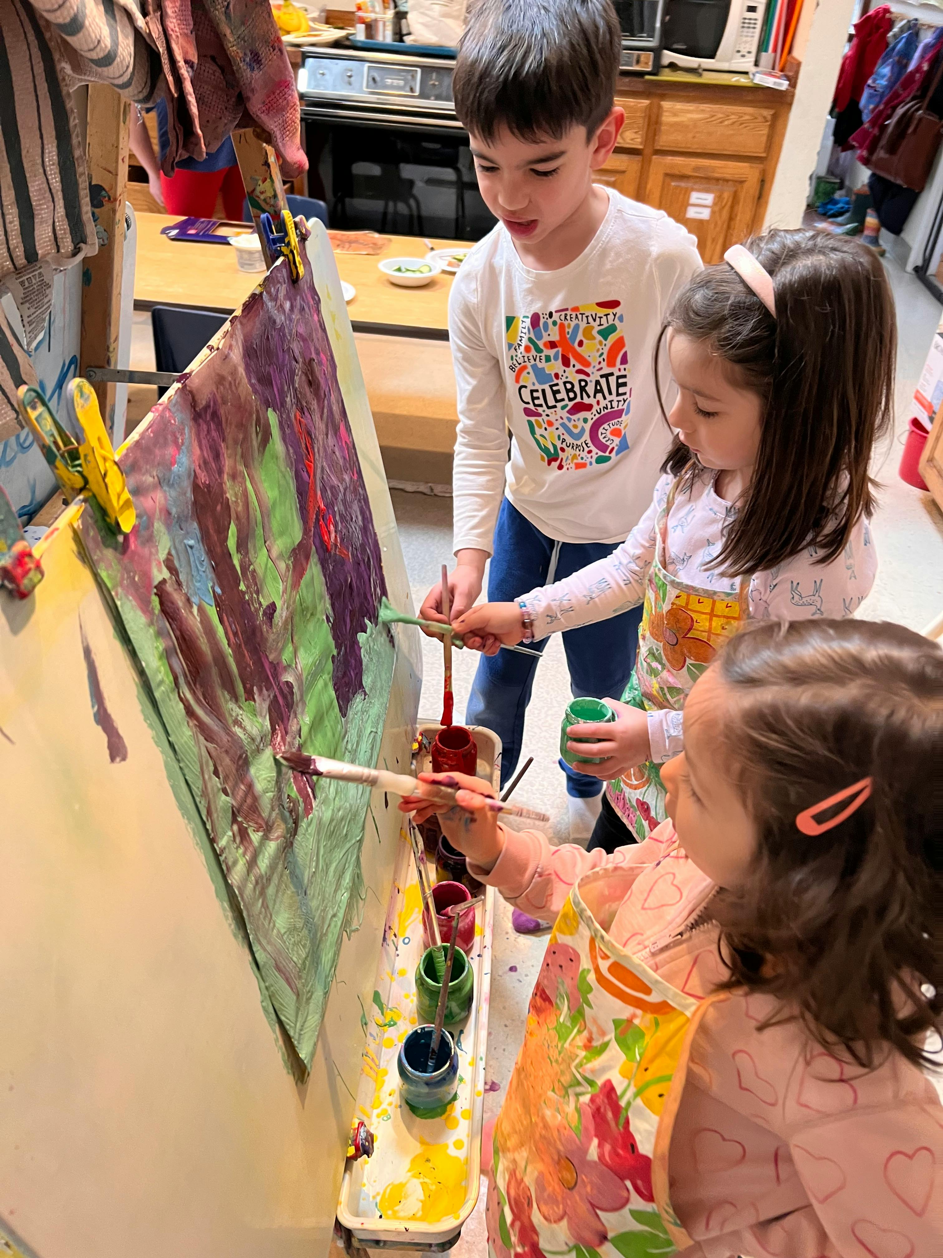 Three children painting on an easel