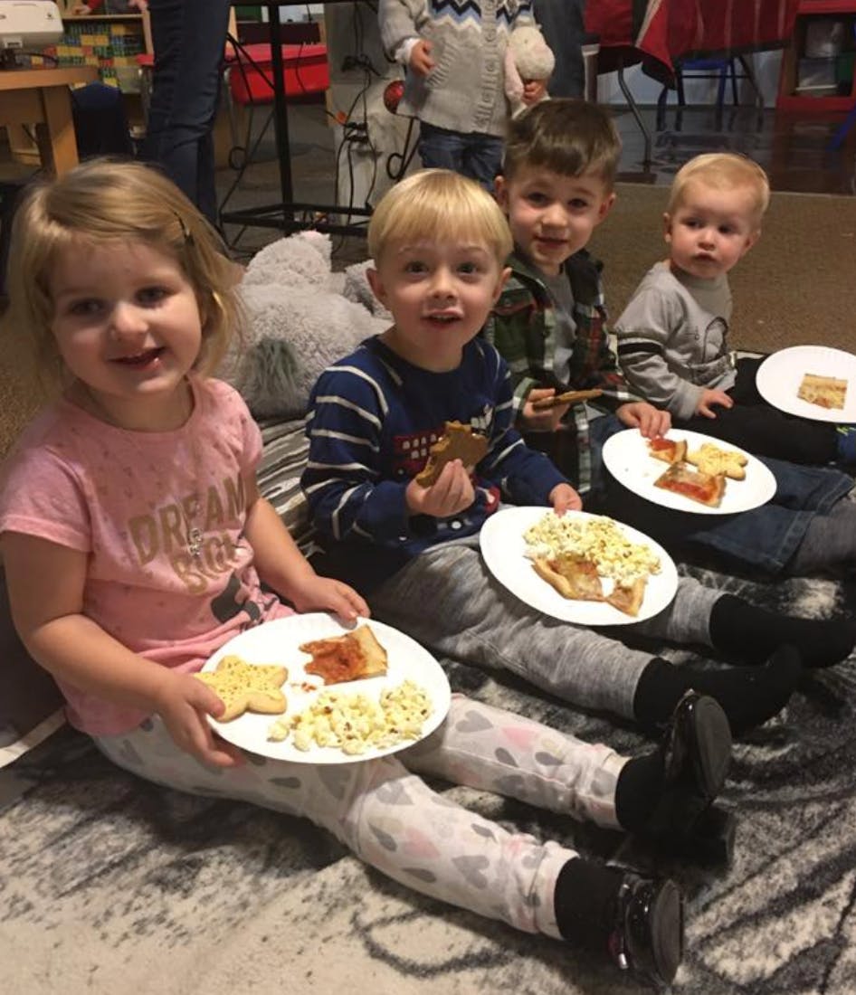 Four children sitting on a rug with plates of food