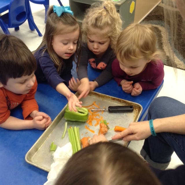 Children peeling vegetables on a tray with an adult
