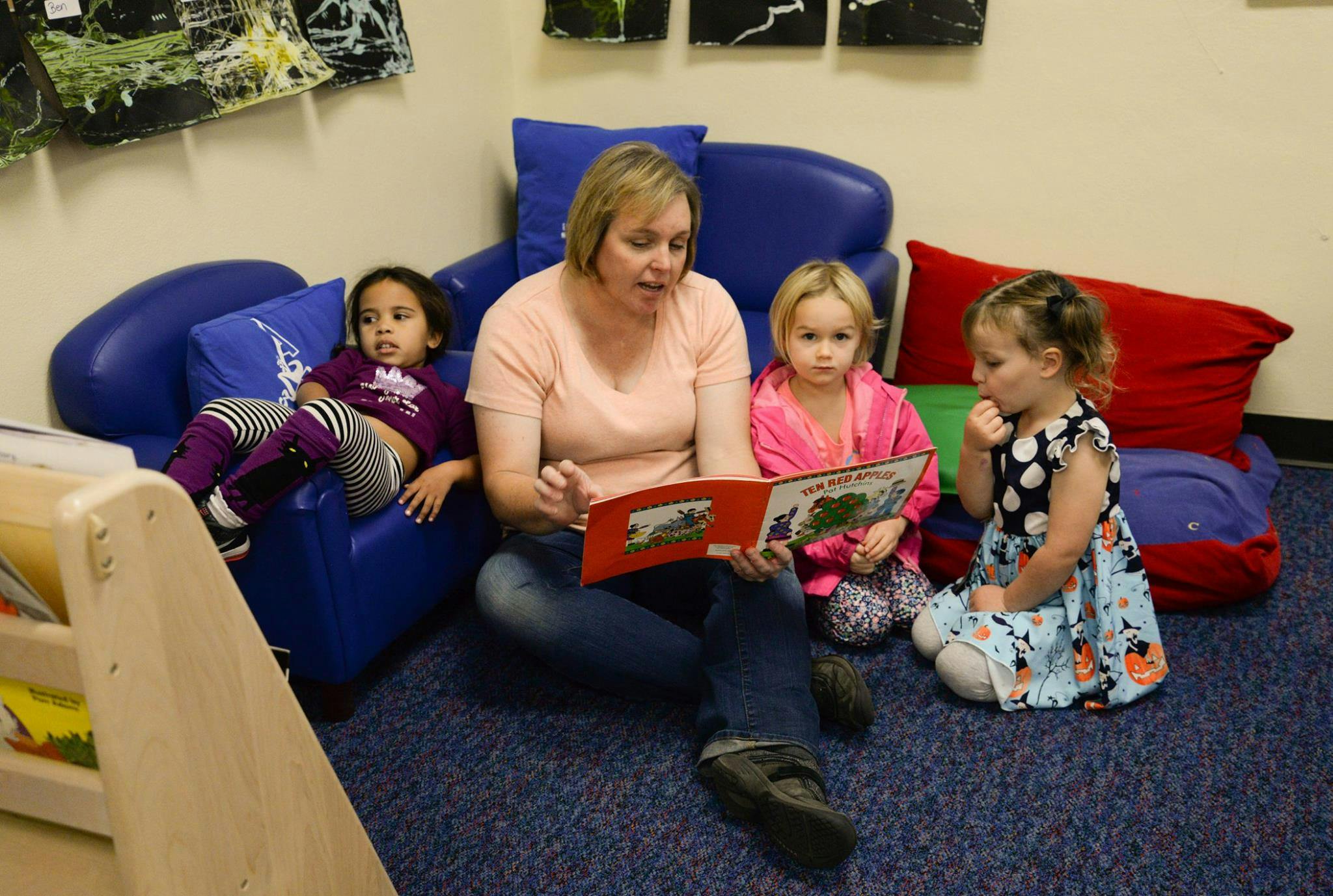 Person reading a book to three children in a classroom